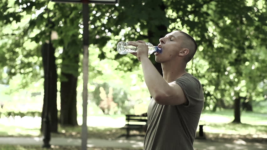 Basketball player drinking water on court in park
