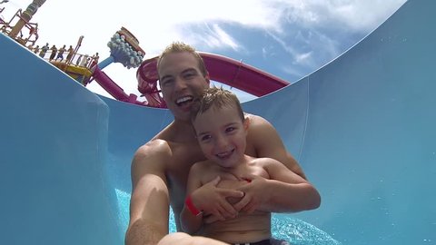 Attractive athletic and healthy father going down a bright colored water slide with his young son on a clear beautiful Summer afternoon.