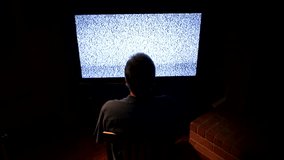 A Man Sits Alone and Watches Static on a TV in a Darkened Room.