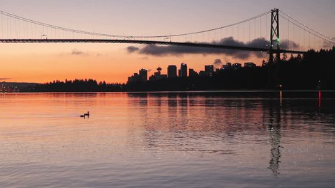 Vancouver. Dawn in Vancouver with the Lion's Gate Bridge crossing to Stanley park and reflecting in Burrard Inlet. The office towers of downtown Vancouver rise in the back ground.
