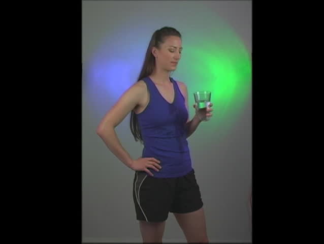 A lovely young woman with long, beautiful, brunette hair and wearing exercise/fitness wear, drinks a glass of water. 
