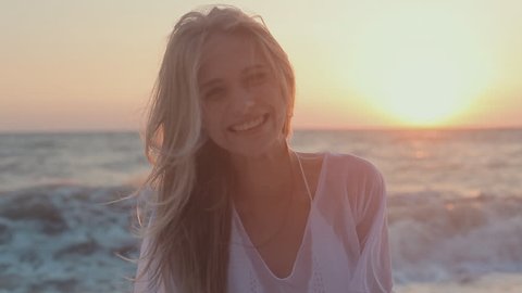 Young seductive girl with long hair in a white tunic smiling and plays the fool at sunset near the sea