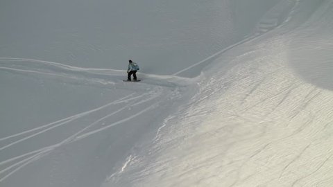 A snowboarder jumps, spins in the air before landing successfully on the slope
