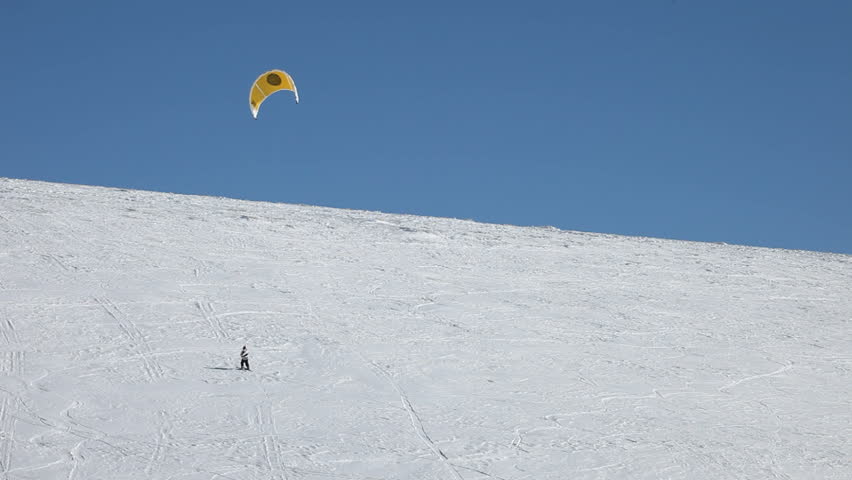 Snowkite riding the mountains of Utah. Bright yellow sail and blue sky above snow covered mountain. High in the mountains of Sanpete County in central Utah.  Skiing up a steep snow covered mountain.