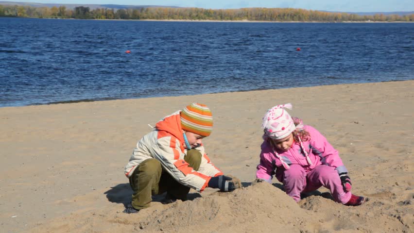 boy and little girl is digging in sand of beach and constructing sand buildings 