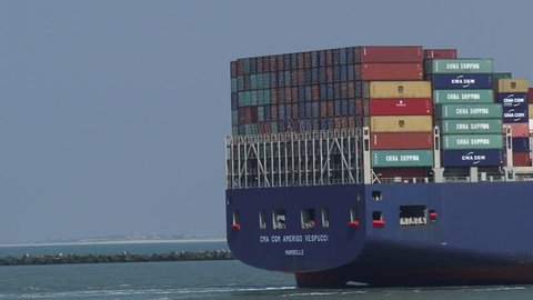 PORT OF ROTTERDAM - JULY 2014: Large container ship CMA CGM Amerigo Vespucci navigates, entering Maasmond, Port of Rotterdam - rear ship. Dutch coastline at horizon.