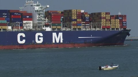 PORT OF ROTTERDAM - JULY 2014: Large container ship CMA CGM Amerigo Vespucci entering Maasmond, Port of Rotterdam. Small fishing boat in front.