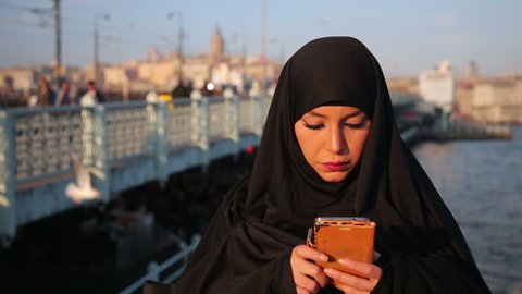Woman dressed with black headscarf, chador using mobile phone