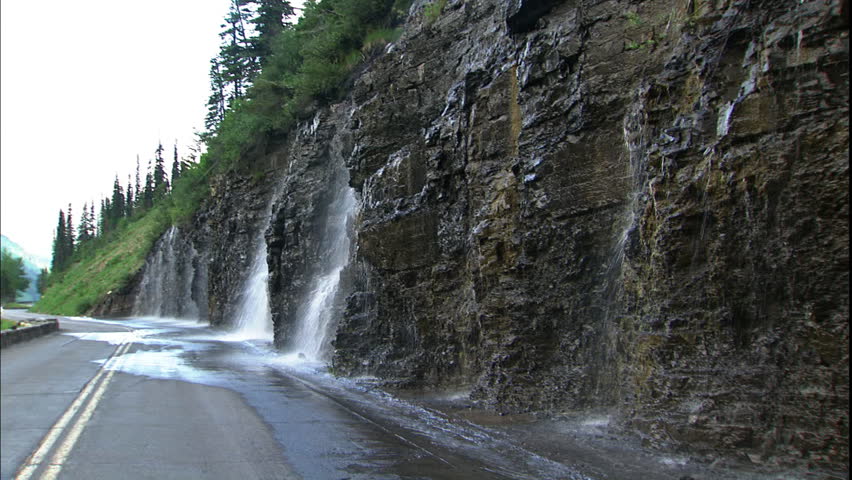 Water falls off the side of a mountain next to a highway