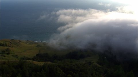 Aerial shot of the cliffs of Big Sur next to the Pacific ocean, covered in fog at dusk