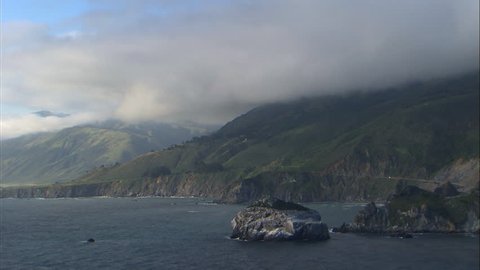 Aerial shot of the mountains of Big Sur next to the Pacific ocean, covered in fog at dusk