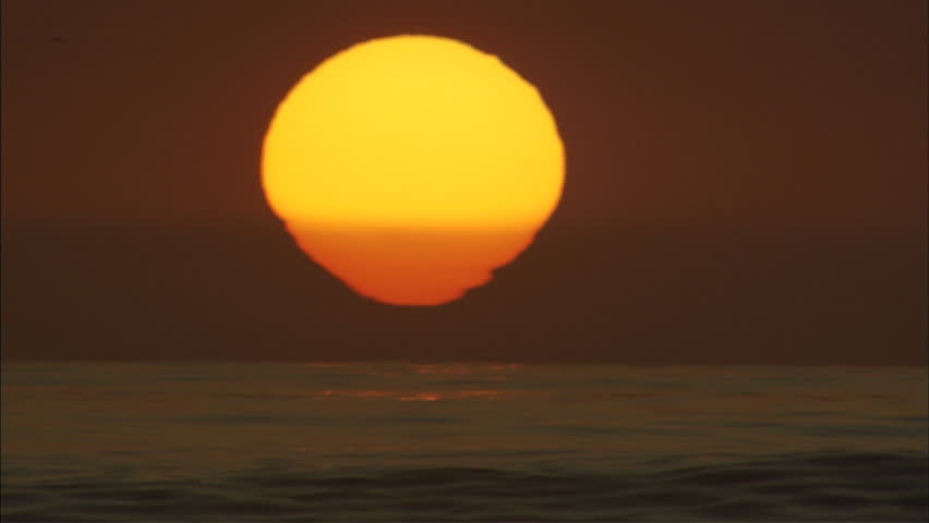 An extreme close up of the evening sun melting into the ocean horizon as a