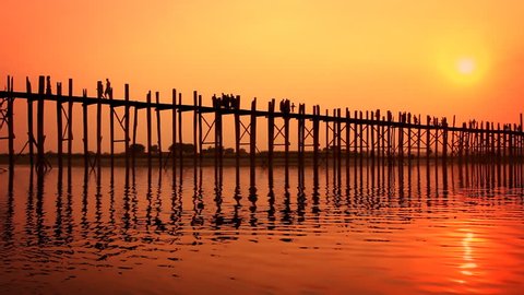 People crossing the U Bein bridge in Amarapura, Myanmar. Dramatic sunset with the bridge and people in silhouette.