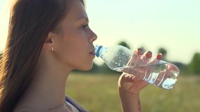 Healthy Teen Girl Drinking Water from the bottle outdoors. Beauty Smiling Young Woman refreshing fresh water over nature background. Slow motion video footage 240 fps. High speed camera shot 1080p