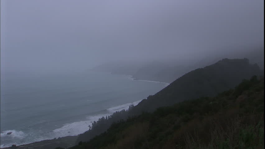 Zoom out of fog hanging over the cliffs of Big Sur in California next to the Pacific