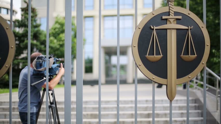 Videographer back behind iron gates of court with symbolic scales and sword