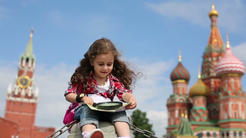 Little girl sits with magnifier and map on Red Square in Moscow