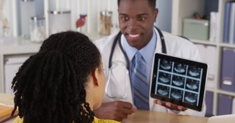 Black physician using tablet to show ultrasound to patient at desk