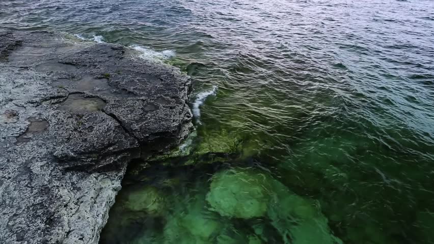 Clear, aquamarine waves on Lake Michigan splash onto the rocky coast of scenic Cave Point in Door County, Wisconsin with early morning light. Looping.