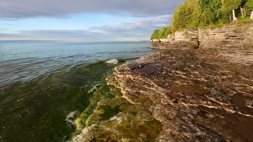 Loop features waves on Lake Michigan gently breaking upon the rocky, wooded coastline of Door County, Wisconsin as white pelicans fly by overhead. 
