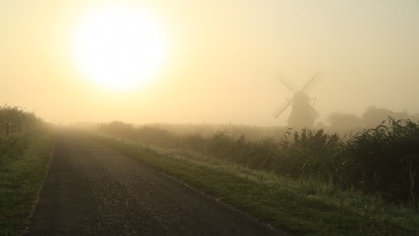 Man running in the foggy, Dutch countryside near a windmill.