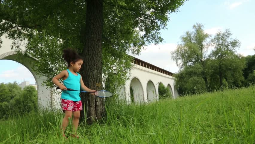 Little cute girl plays with racket and shuttlecock on green grass at summer