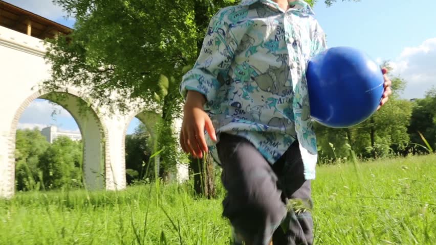 Boy with ball walks on grass and boy and girl walk behind them in summer park