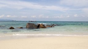 View of white sand, big rock, beach, boat passing by, blue sky with clouds and harmony waves at Lalang Island, Lumut, Perak, Malaysia, facing to Straits of Malacca