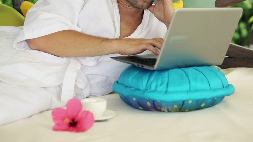 Man with laptop having break for coffee and relax on gazebo bed
