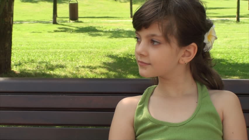 Portrait Of A Beautiful Little Girl Sitting On A Bench In Park, Outdoors, Tilt