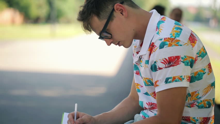 Young man writing in notebook in city park
