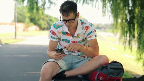 Young man texting, using smartphone in city park
