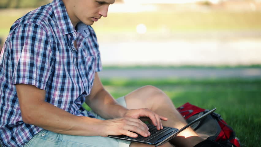 Young student working on laptop in city park
