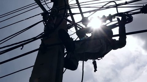 Silhouette of an electrician climbing a newly installed utility pole
