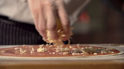 Extreme close up of unrecognizable man putting cheese topping on his pizza base