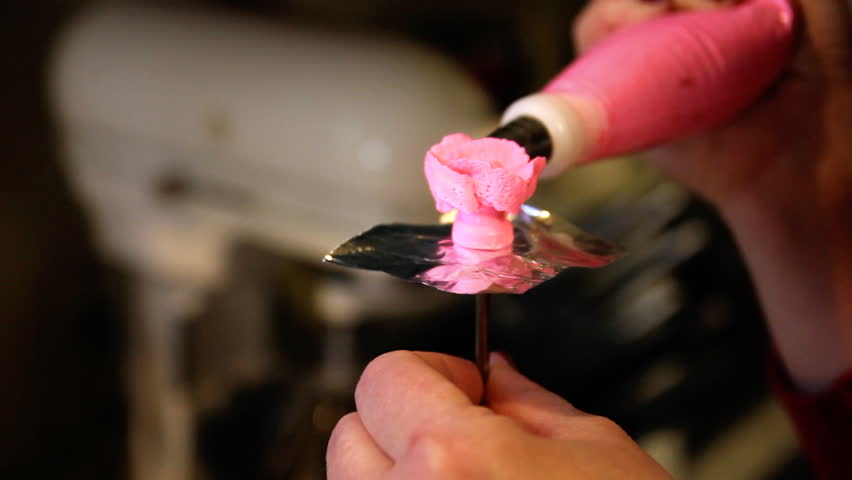 A woman creates flowers for a cake out of frosting.