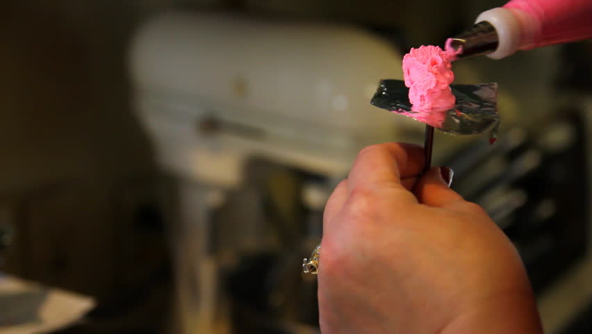 A woman creates flowers for a cake out of frosting.