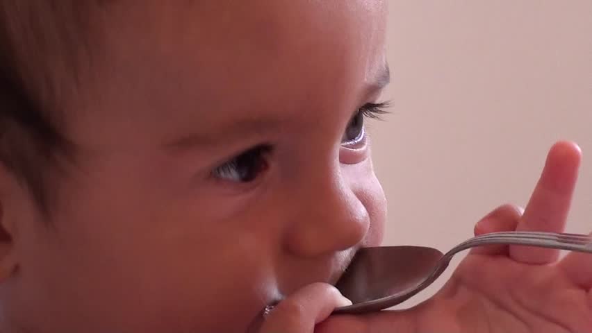 Funny baby with a bruise on his forehead plays with a metal spoon, zoom out