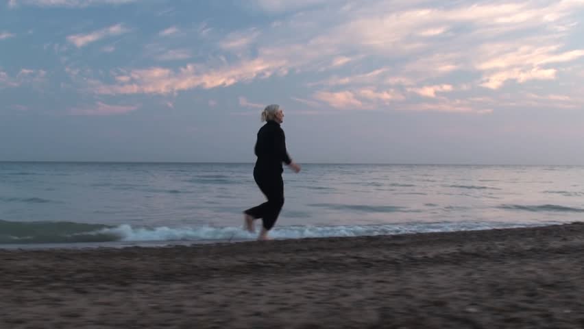 Woman in black run through lake beach 2. Tracking movements with Steadicam.