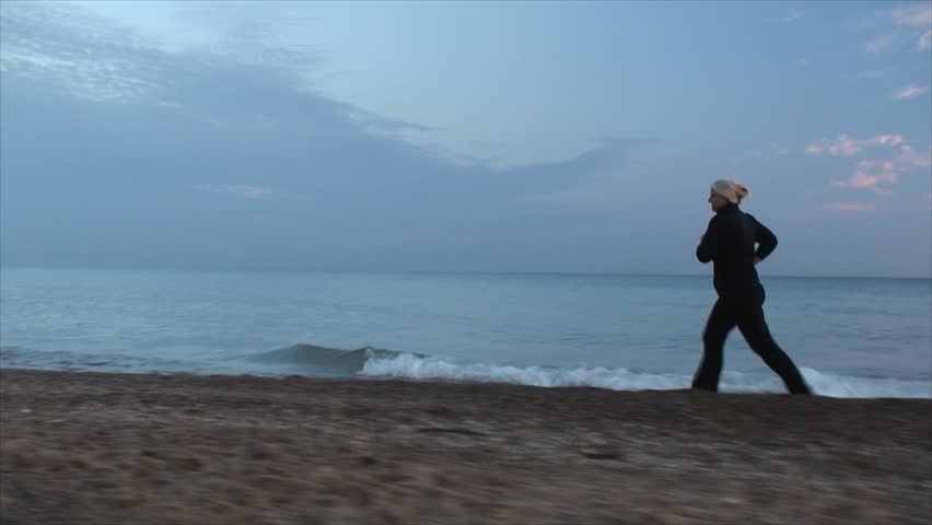 Woman in black run through lake beach. Tracking movements with Steadicam.