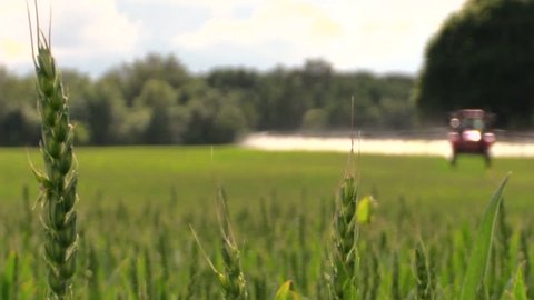 village tractor spraying green crop field on farm sunny day. Focus change. Shot on Canon XA25. Full HD 1080p. Progressive scan 25fps. Tripod