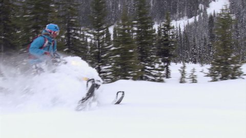 A man on a snowmobile rides through the forest in slow motion