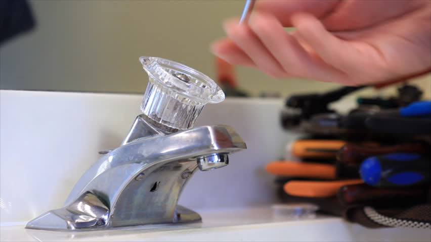 A man using pliers to remove the internal cartridge of a broken faucet handle.