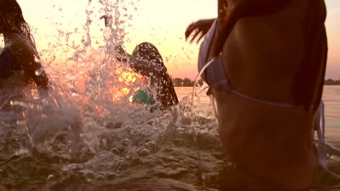 Group of happy teen girls playing in water at the beach. Beauty joyful teenager friends having fun, dancing and spraying over summer sunset. Beach party. Sun flare. Slow motion. Summertime. HD 1080p