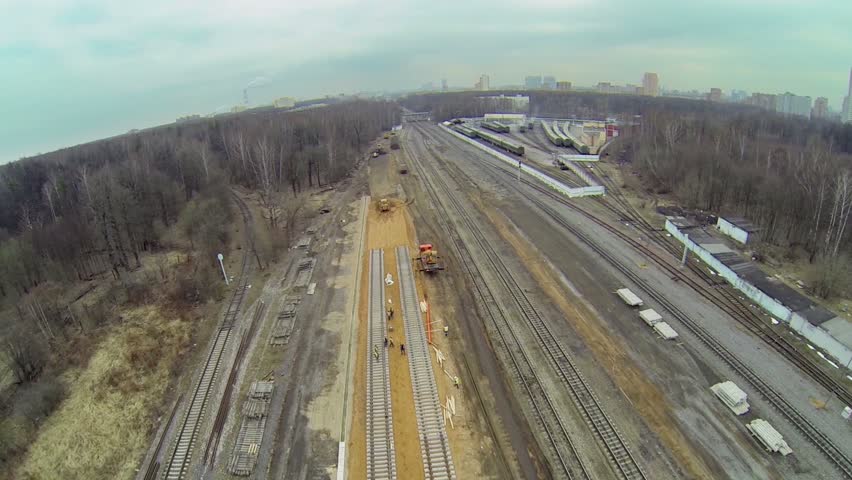 Construction site of railroad tracks among forest with city at horizon. Aerial view