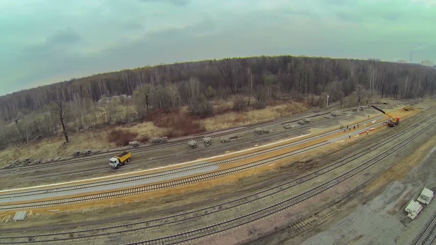 Truck and crane at building site of railway tracks among forest at spring cloudy day. Aerial view