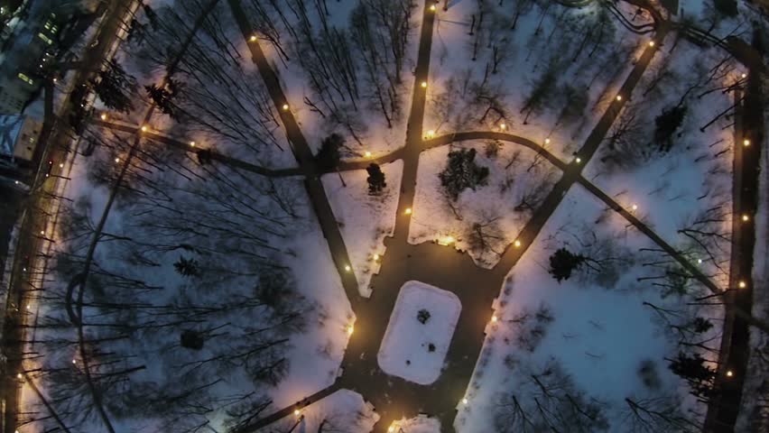 Alleys with illumination in small park at evening. Aerial view
