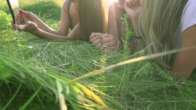 Girls with a touchscreen lying on the grass in sunny lights. Happy teen friends using touchpad outdoors. Lens flare. Slow motion video footage 240 fps . High speed camera shot. Full HD 1080p
