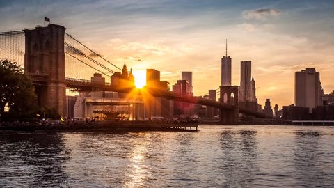 New York timelapse with Brooklyn Bridge going through sunset, twilight and night, while boats sail the East River.