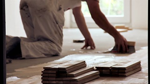 Carpenter worker installing glue for wood parquet board during flooring